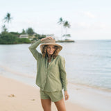 Woman wearing loose button up with smocked tube top and short in medium green linen.