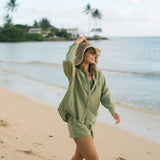 Woman wearing loose button up with smocked tube top and short in medium green linen.