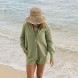 Woman wearing loose button up with smocked tube top and short in medium green linen.