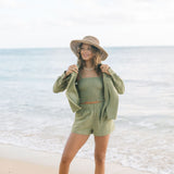 Woman wearing loose button up with smocked tube top and short in medium green linen.