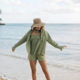Woman wearing loose button up with smocked tube top and short in medium green linen.