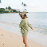 Woman wearing loose button up with smocked tube top and short in medium green linen.