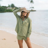 Woman wearing loose button up with smocked tube top and short in medium green linen.