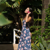 woman with black hair wearing a maxi tiered dress in a navy color with pink hibiscus blossoms