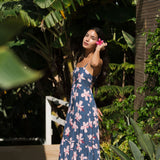 woman with black hair wearing a maxi tiered dress in a navy color with pink hibiscus blossoms