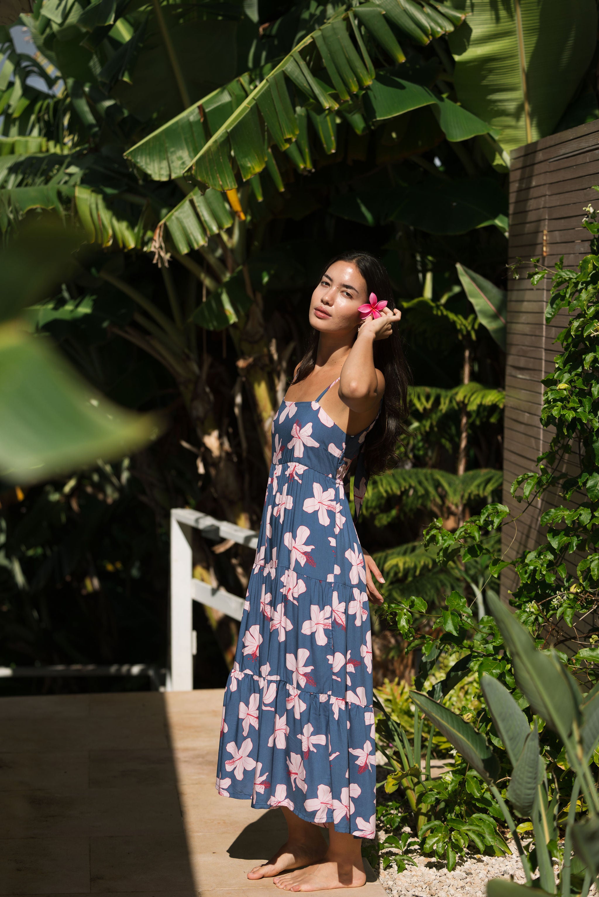 woman with black hair wearing a maxi tiered dress in a navy color with pink hibiscus blossoms