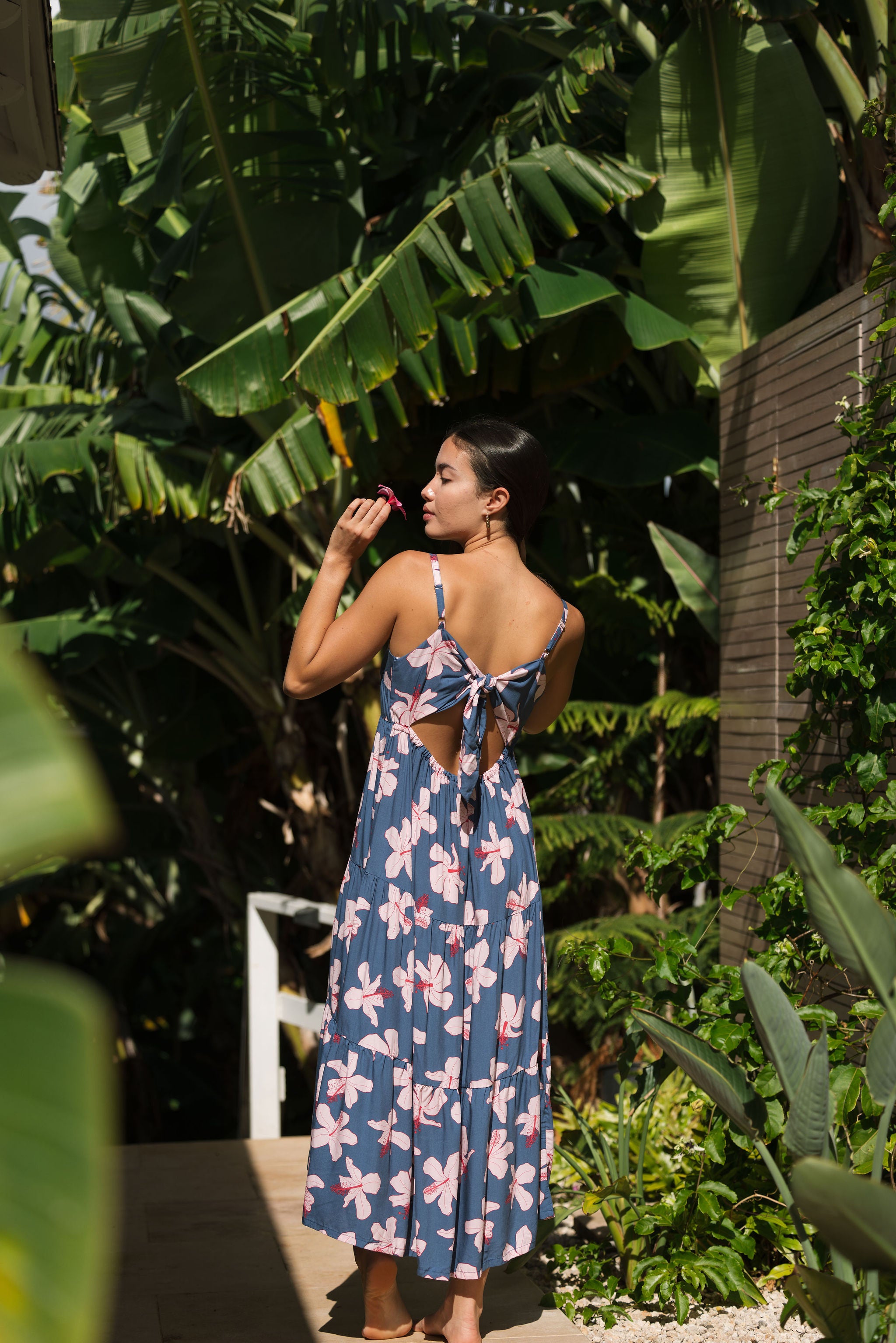 woman with black hair wearing a maxi tiered dress in a navy color with pink hibiscus blossoms