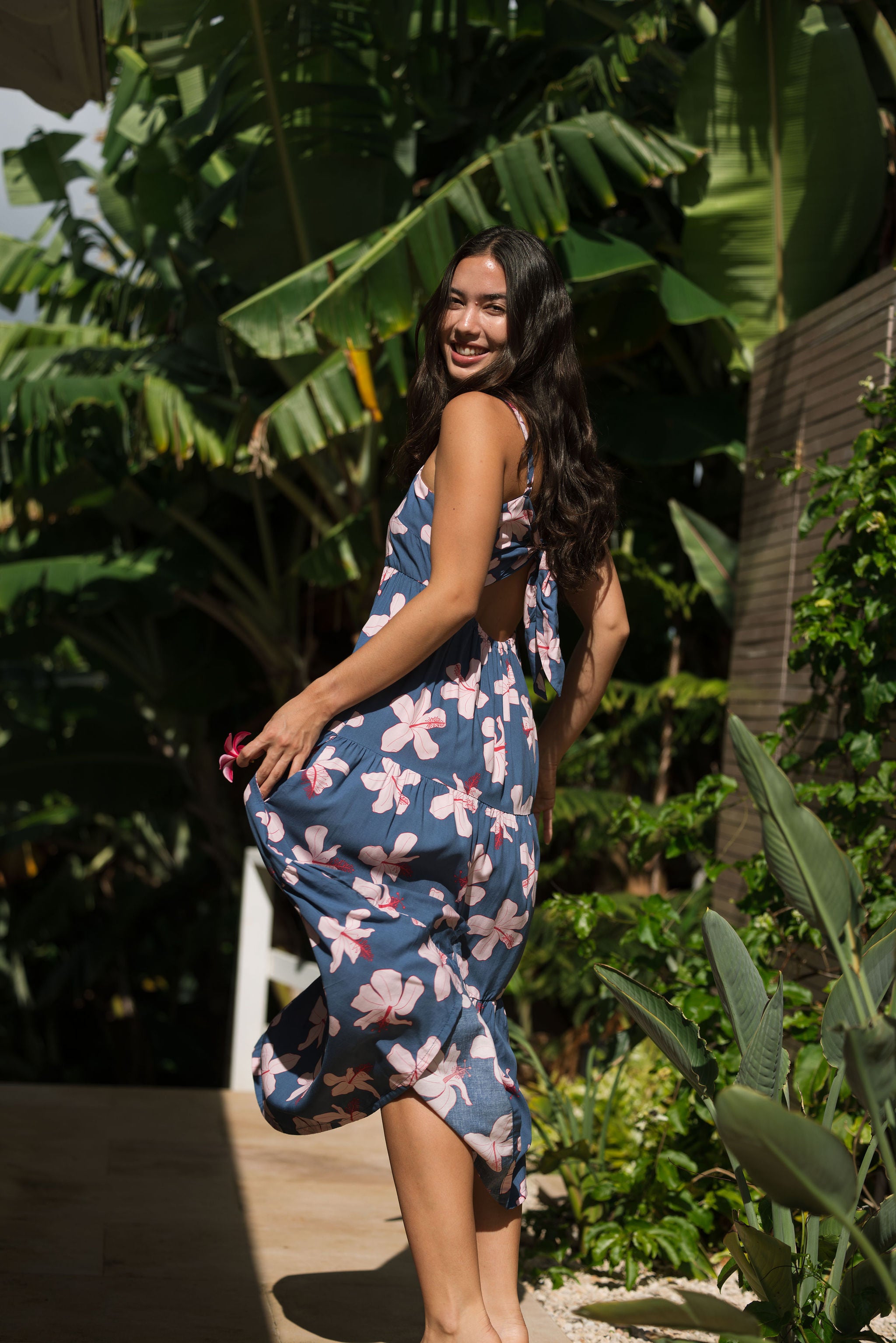 woman with black hair wearing a maxi tiered dress in a navy color with pink hibiscus blossoms