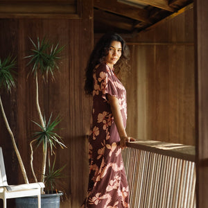 woman with brown hair wearing a brown colored maxi button up dress with light pink lei awapuhi print