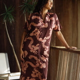 woman with brown hair wearing a brown colored maxi button up dress with light pink lei awapuhi print