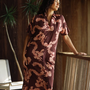 woman with brown hair wearing a brown colored maxi button up dress with light pink lei awapuhi print