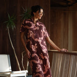 woman with brown hair wearing a brown colored maxi button up dress with light pink lei awapuhi print