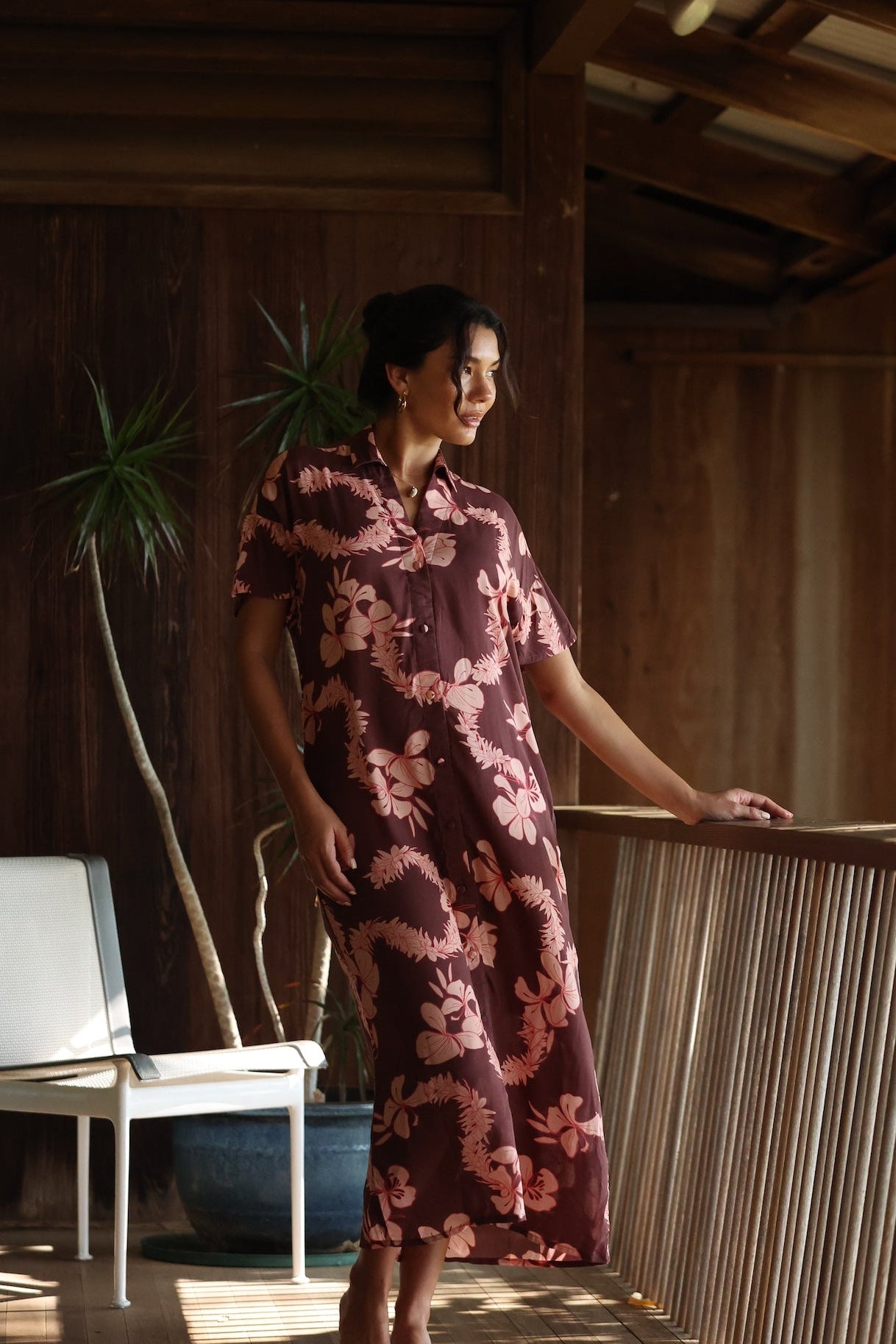 woman with brown hair wearing a brown colored maxi button up dress with light pink lei awapuhi print