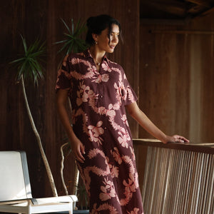 woman with brown hair wearing a brown colored maxi button up dress with light pink lei awapuhi print
