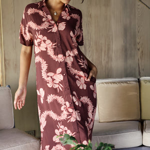 woman with brown hair wearing a brown colored maxi button up dress with light pink lei awapuhi print