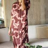 woman with brown hair wearing a brown colored maxi button up dress with light pink lei awapuhi print