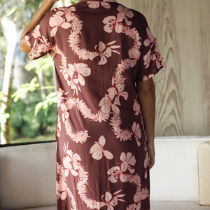 woman with brown hair wearing a brown colored maxi button up dress with light pink lei awapuhi print