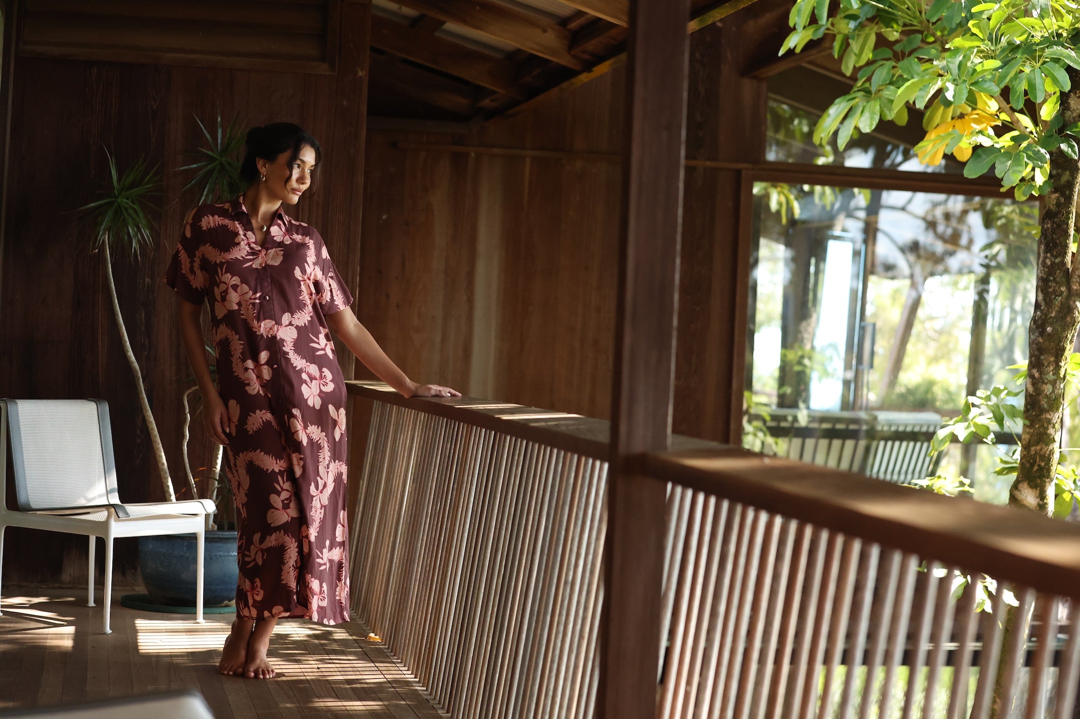woman with brown hair wearing a brown colored maxi button up dress with light pink lei awapuhi print