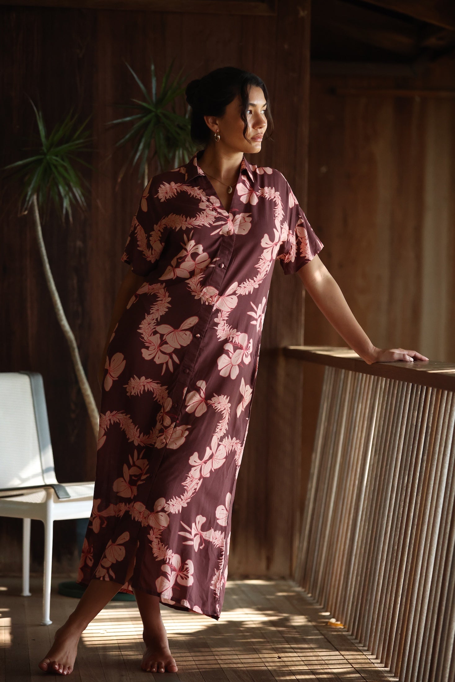 woman with brown hair wearing a brown colored maxi button up dress with light pink lei awapuhi print