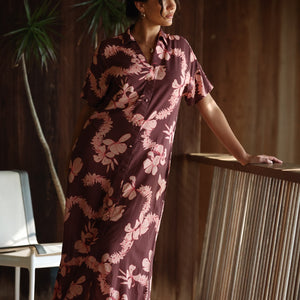 woman with brown hair wearing a brown colored maxi button up dress with light pink lei awapuhi print