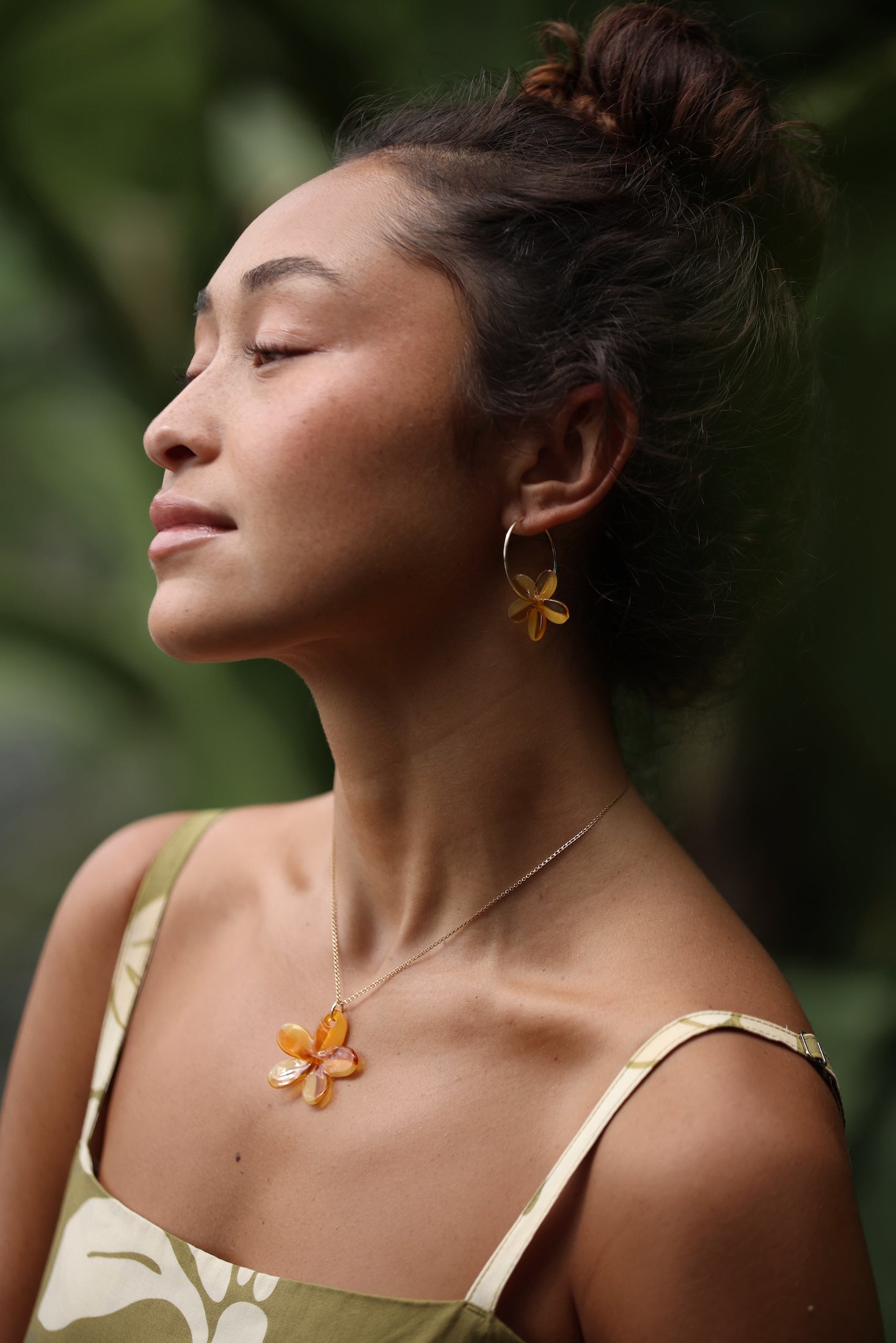 woman with brown hair wearing yellow glass plumeria necklace and earrings