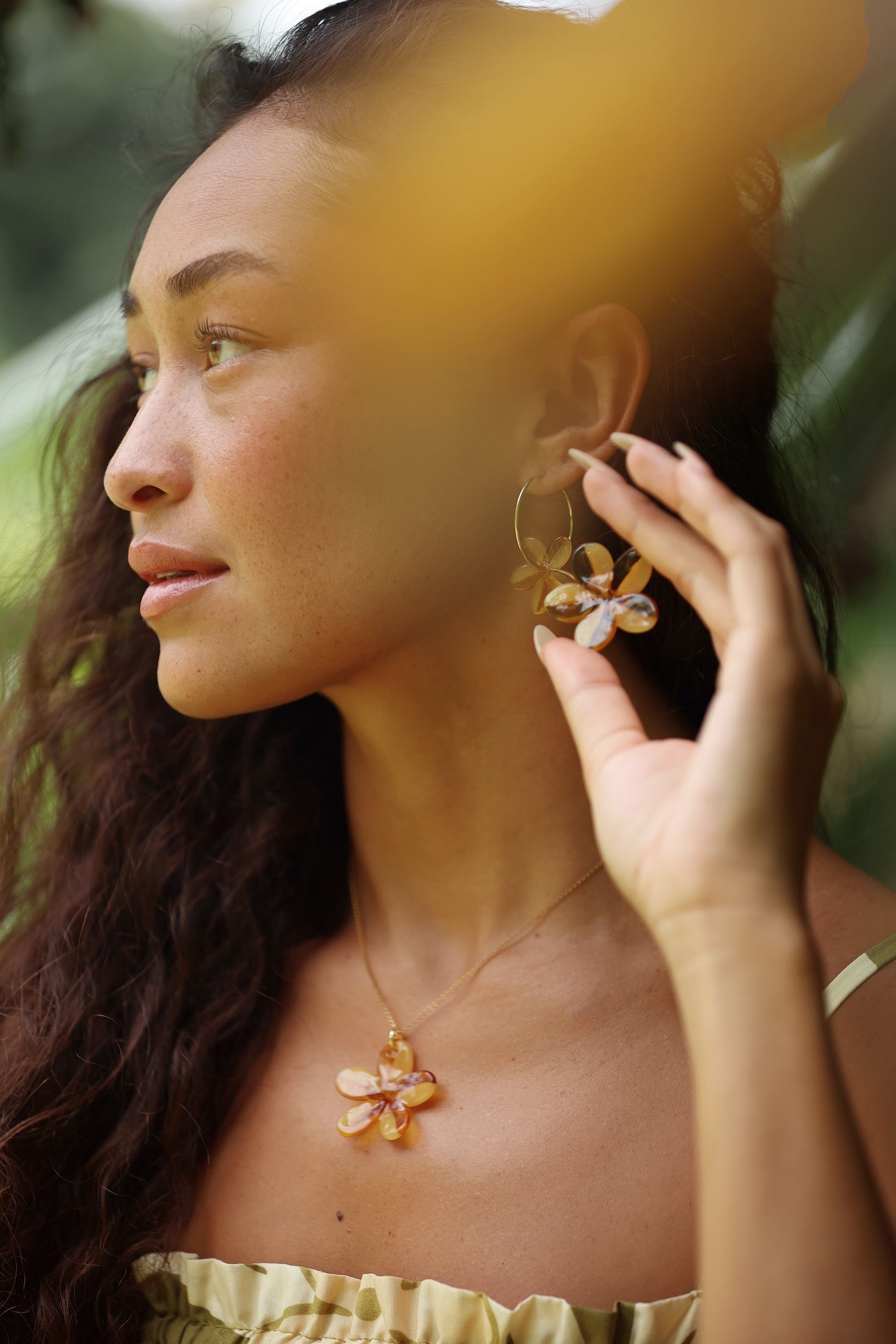 woman with brown hair wearing yellow glass plumeria necklace and earrings