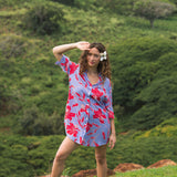 woman with brown hair wearing a mid length button up dress with periwinkle background and bright red hibiscus print.
