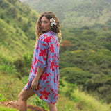 woman with brown hair wearing a mid length button up dress with periwinkle background and bright red hibiscus print.