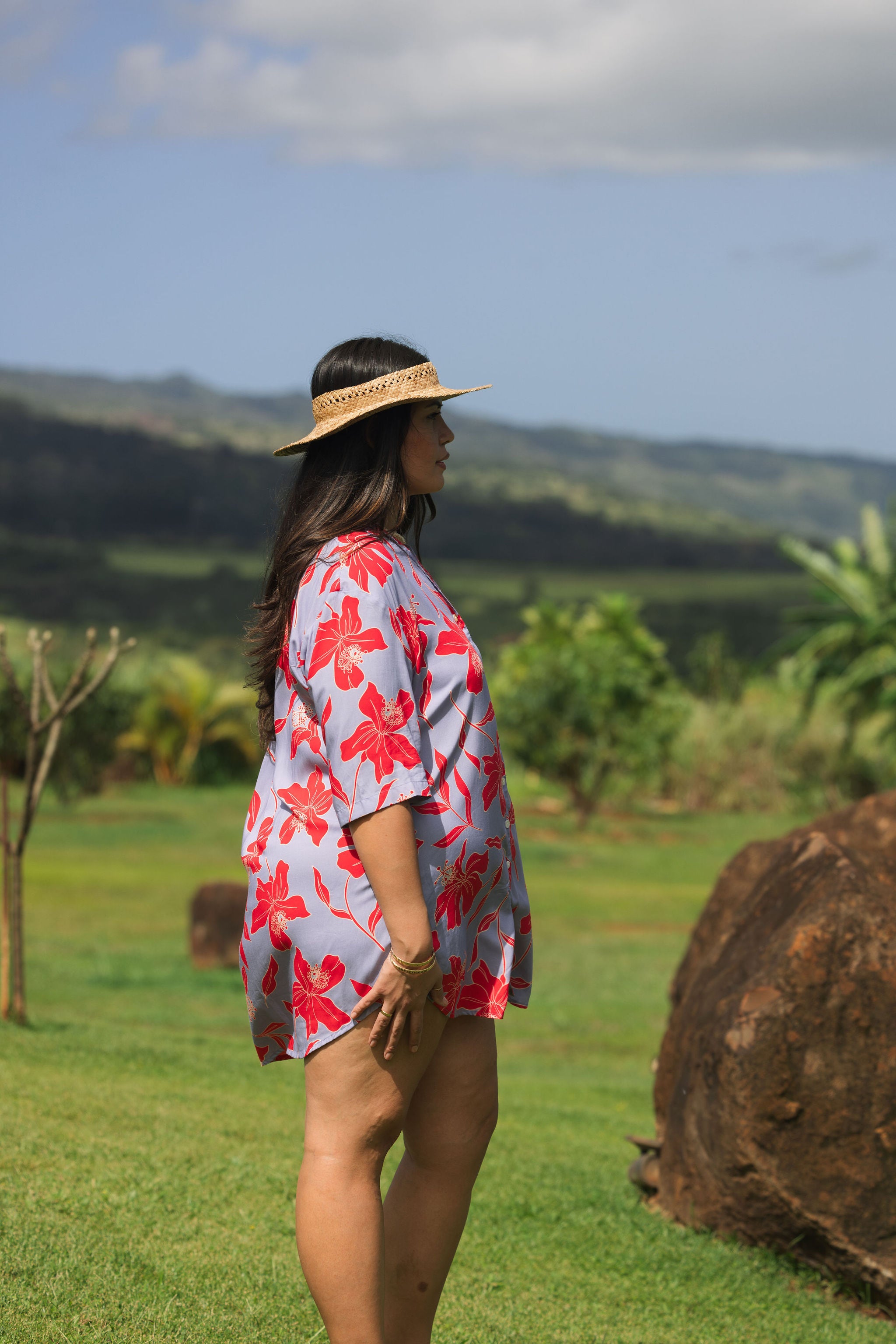 woman with brown hair wearing a mid length button up dress with periwinkle background and bright red hibiscus print.