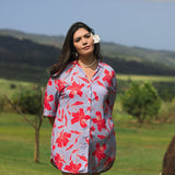 woman with brown hair wearing a mid length button up dress with periwinkle background and bright red hibiscus print.