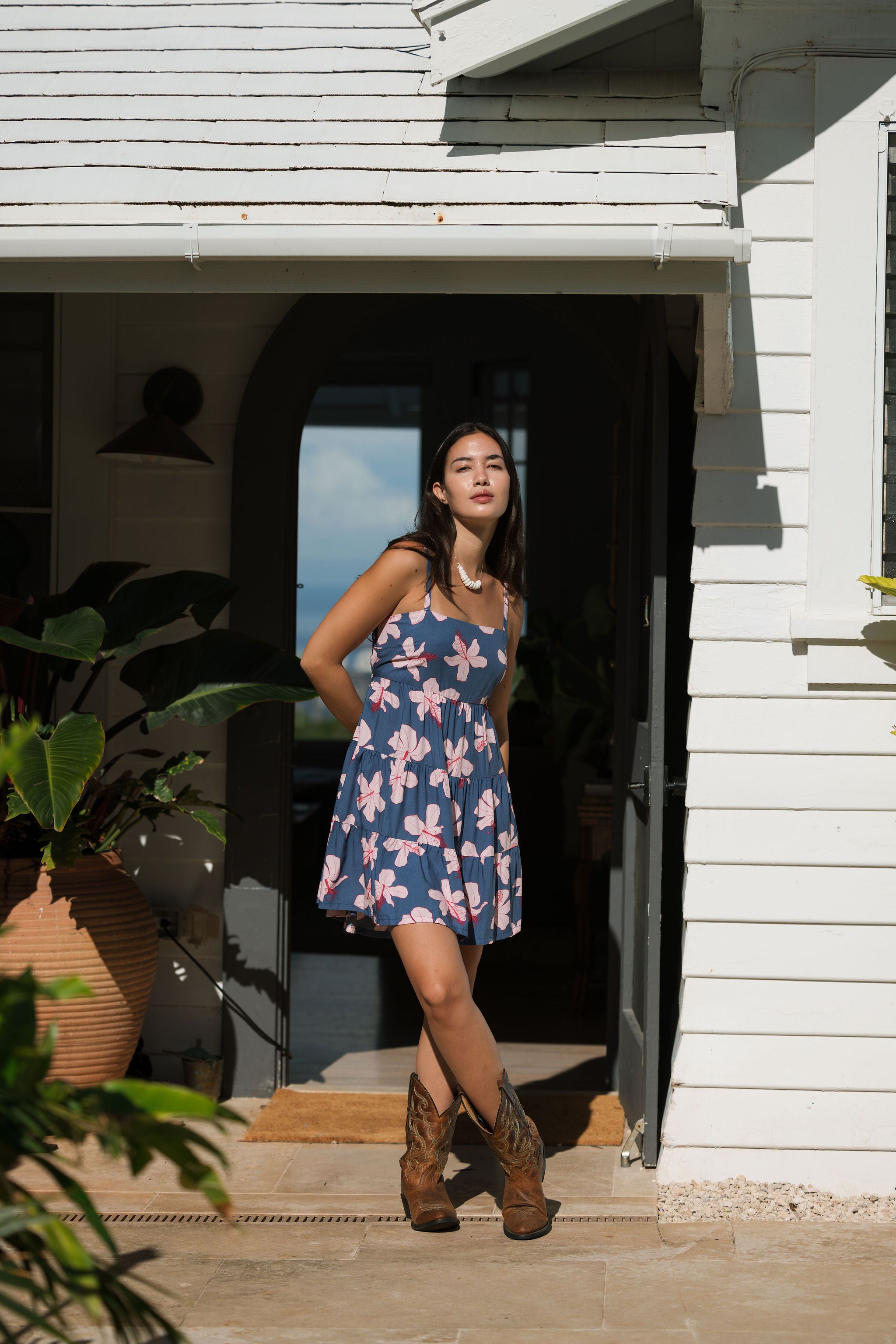 woman with black hair wearing a mini tiered dress with tie back in a navy color with pink hibiscus blossoms