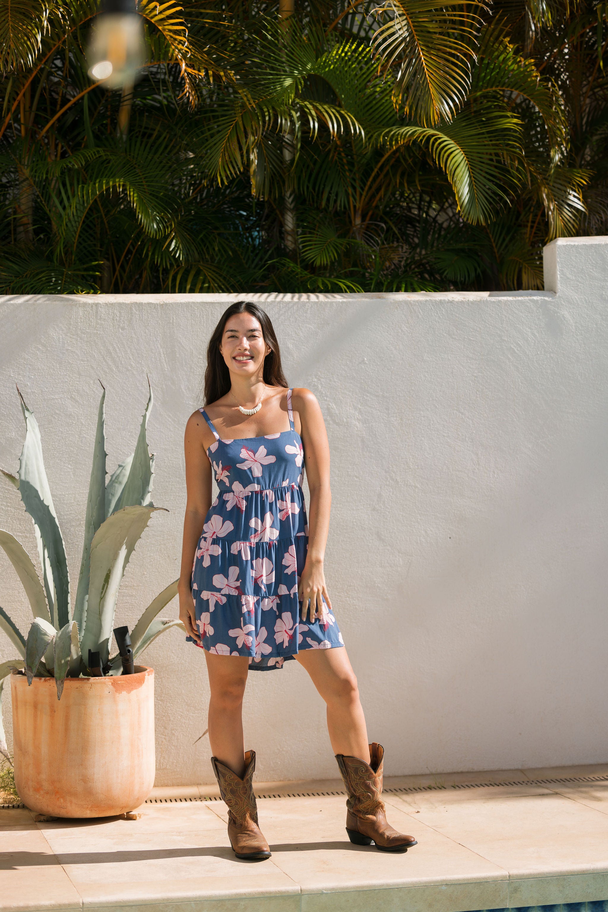 woman with black hair wearing a mini tiered dress with tie back in a navy color with pink hibiscus blossoms