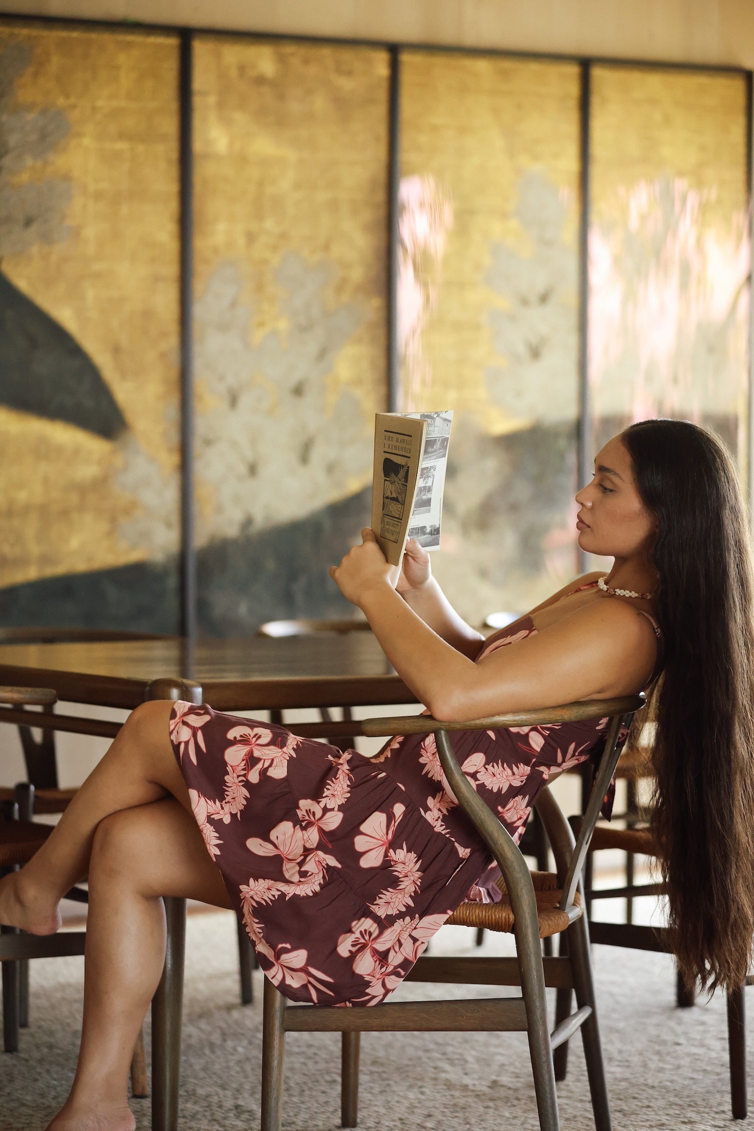 woman with brown hair wearing a brown colored tie back mini dress  with light pink lei awapuhi print
