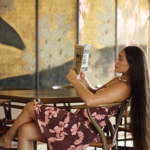 woman with brown hair wearing a brown colored tie back mini dress  with light pink lei awapuhi print