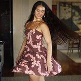 woman with brown hair wearing a brown colored tie back mini dress  with light pink lei awapuhi print