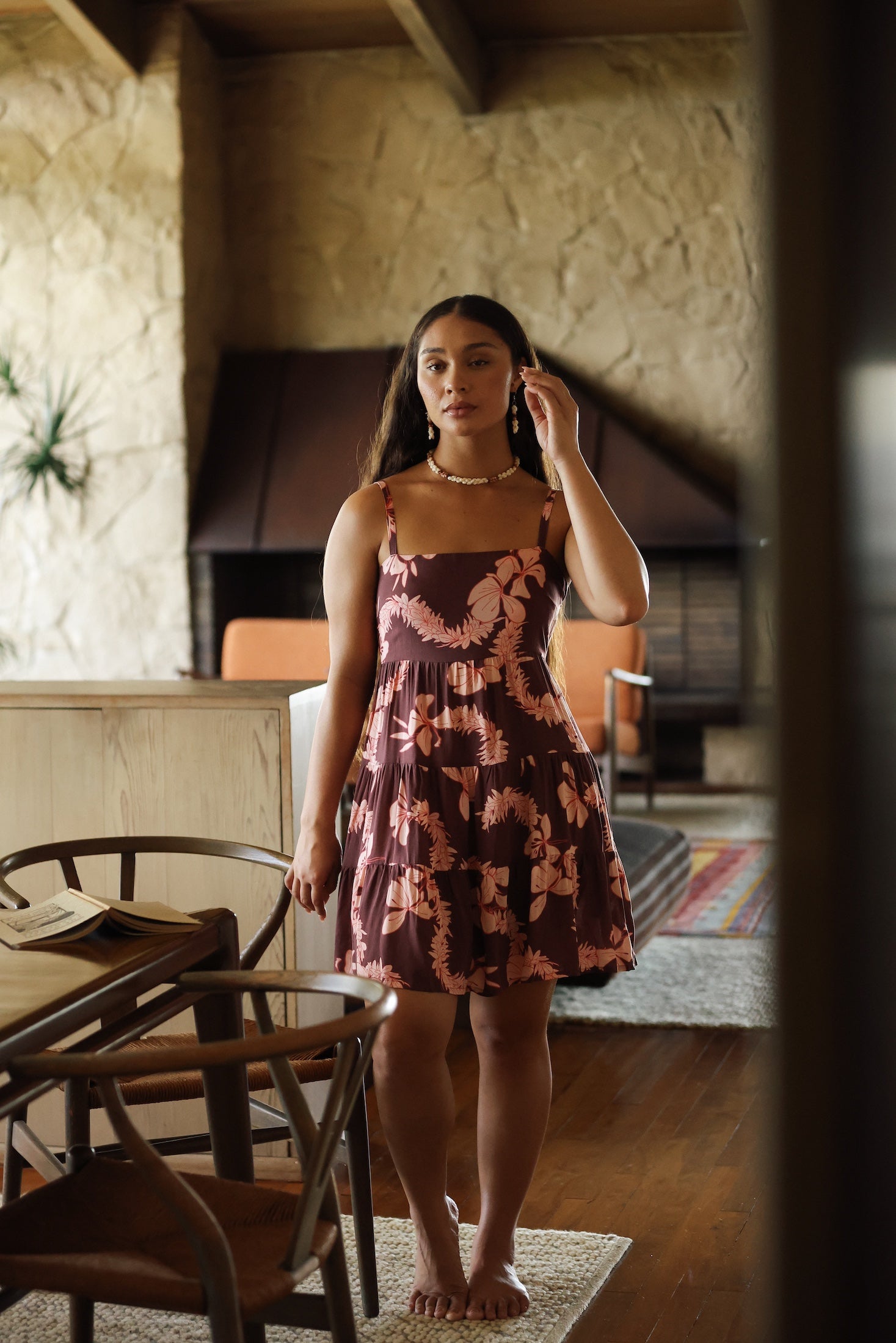 woman with brown hair wearing a brown colored tie back mini dress  with light pink lei awapuhi print