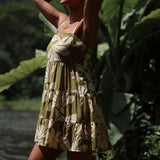 woman with brown hair wearing a mini dress with a tie back in a green color with naupaka pattern throughout.