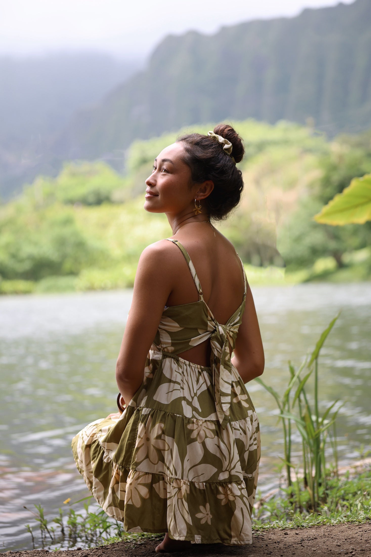 woman with brown hair wearing a mini dress with a tie back in a green color with naupaka pattern throughout.