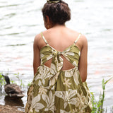 woman with brown hair wearing a mini dress with a tie back in a green color with naupaka pattern throughout.