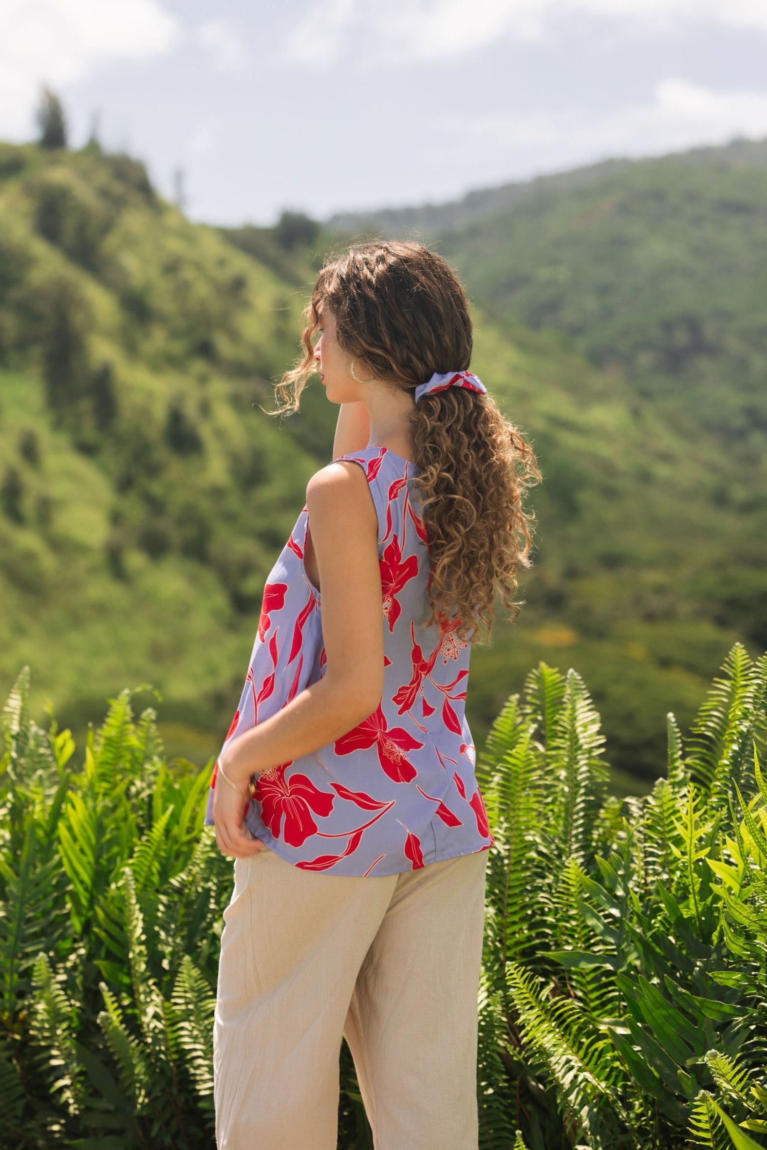 woman with brown hair wearing a sleeveless blouse with periwinkle background and bright red hibiscus print.