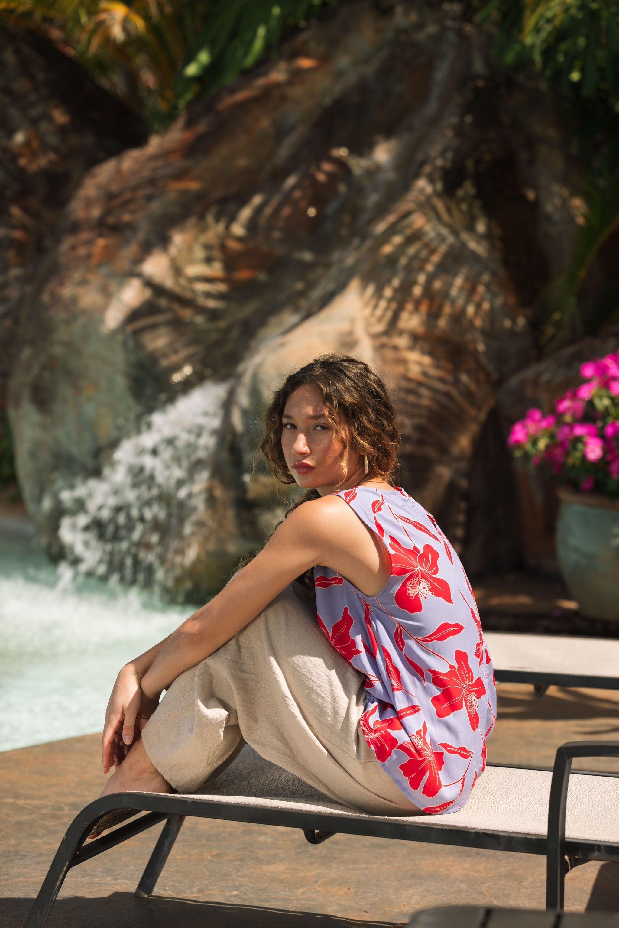 woman with brown hair wearing a sleeveless blouse with periwinkle background and bright red hibiscus print.