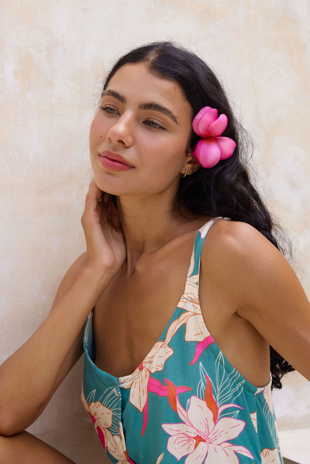 woman with brown hair wearing a romper in teal with large cream colored orchids.