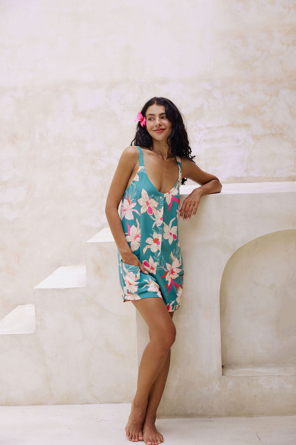 woman with brown hair wearing a romper in teal with large cream colored orchids.