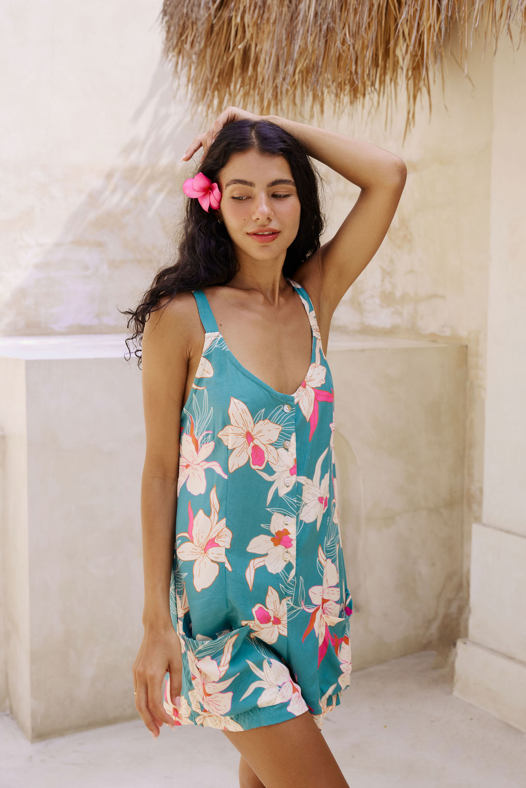 woman with brown hair wearing a romper in teal with large cream colored orchids.