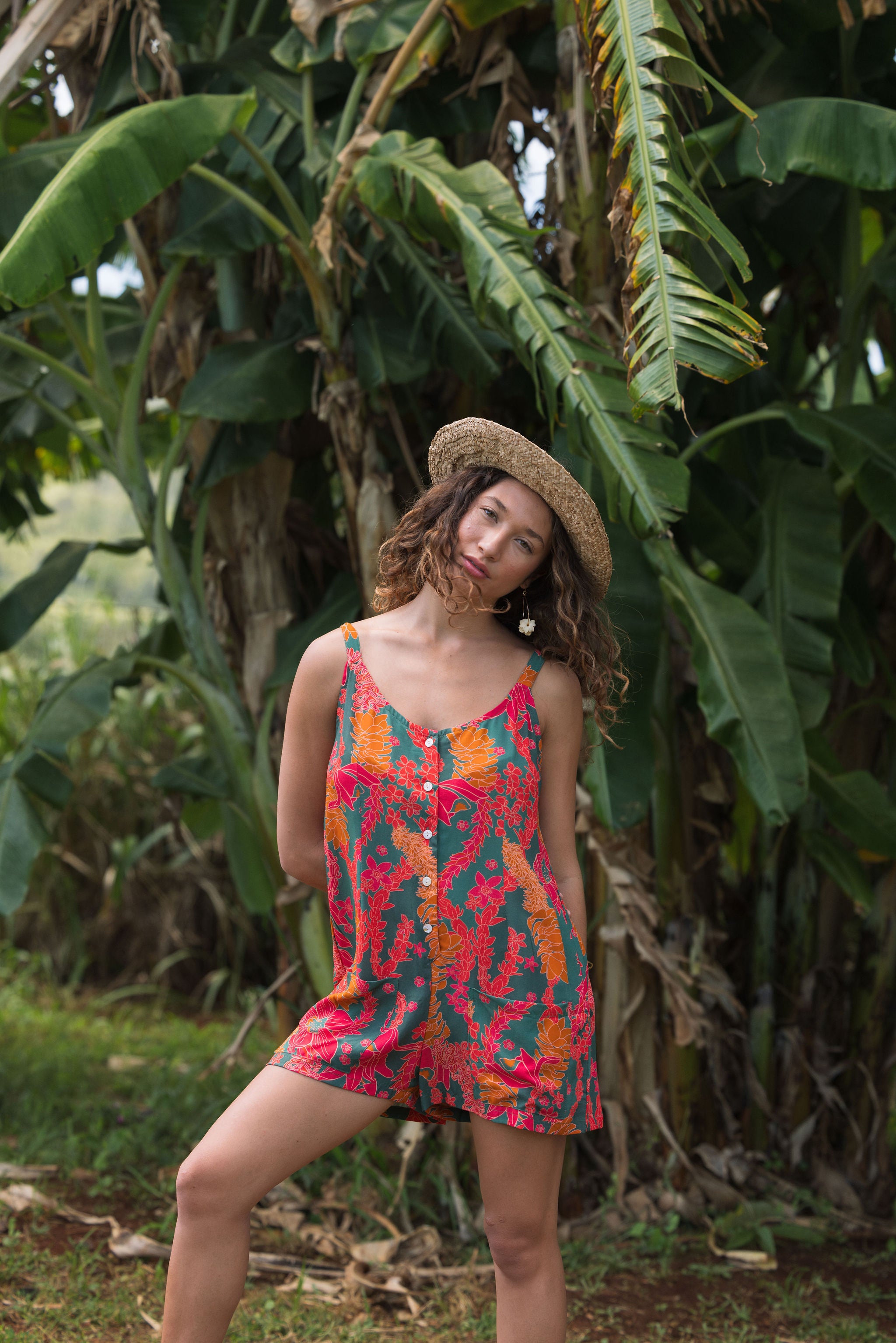 woman with brown hair wearing a colorful romper with tropical lei print