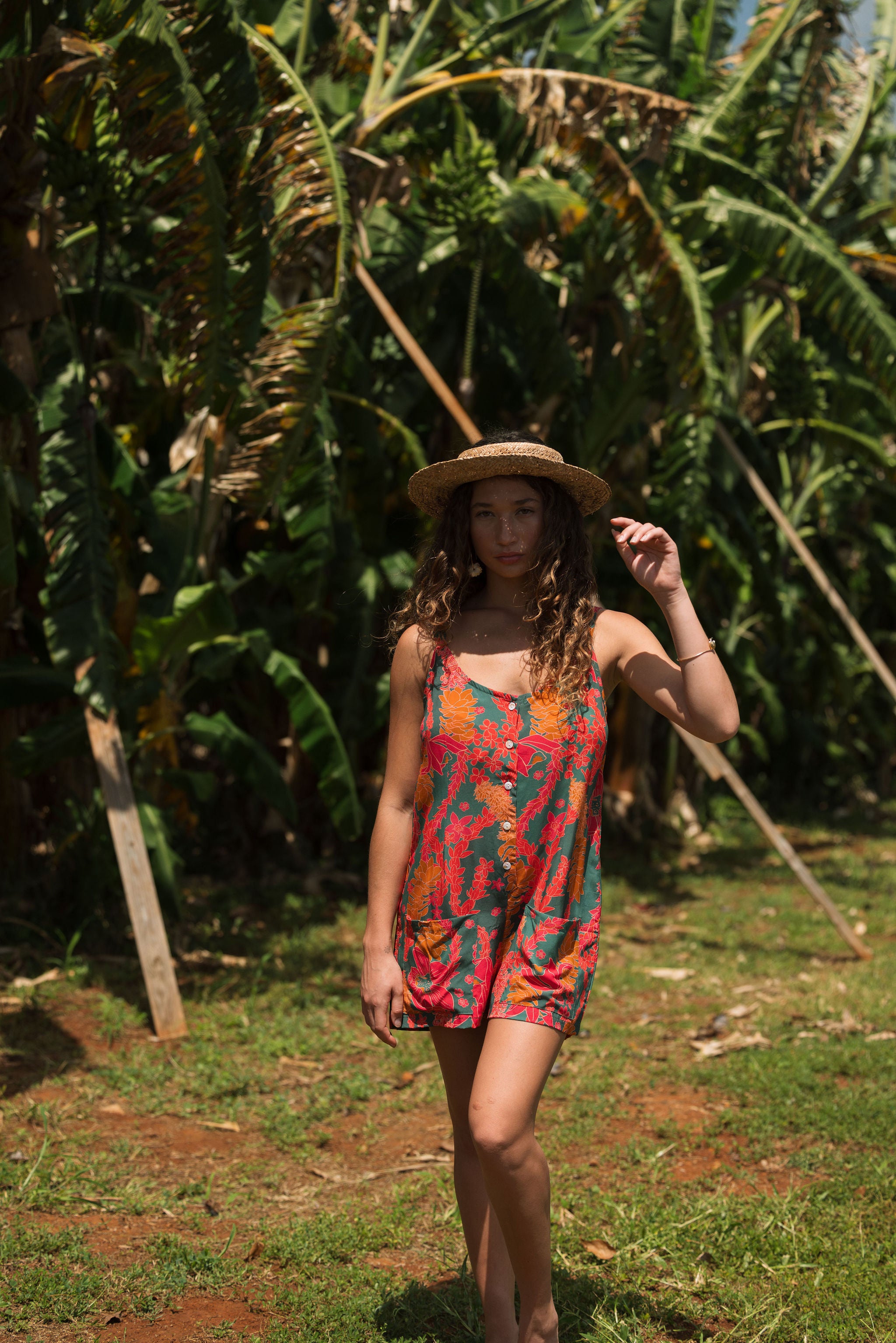 woman with brown hair wearing a colorful romper with tropical lei print