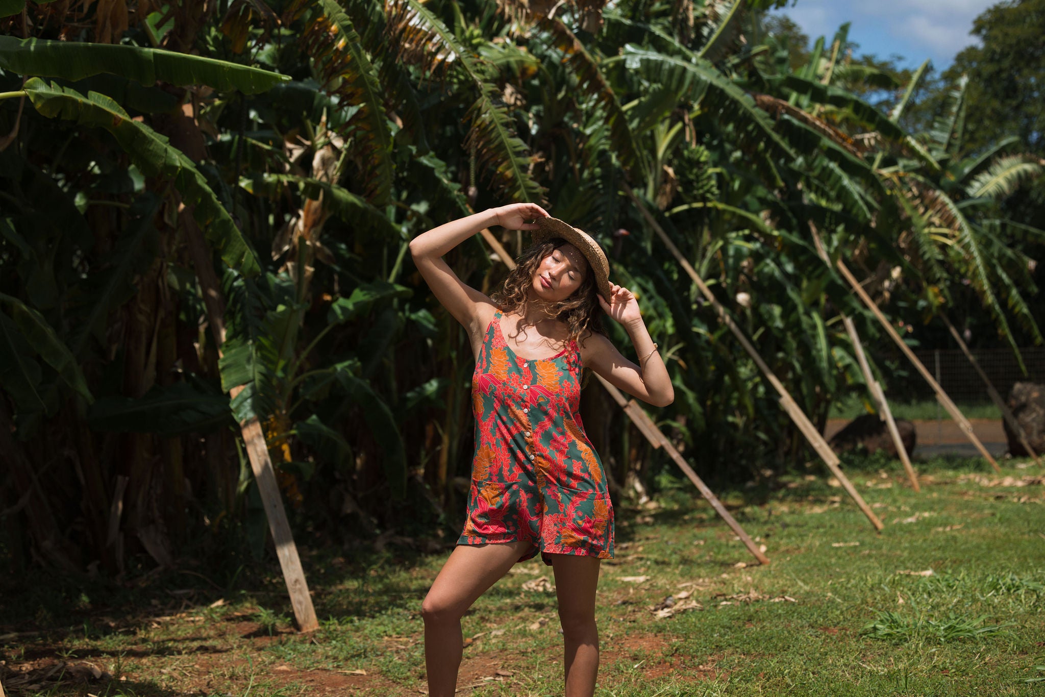 woman with brown hair wearing a colorful romper with tropical lei print