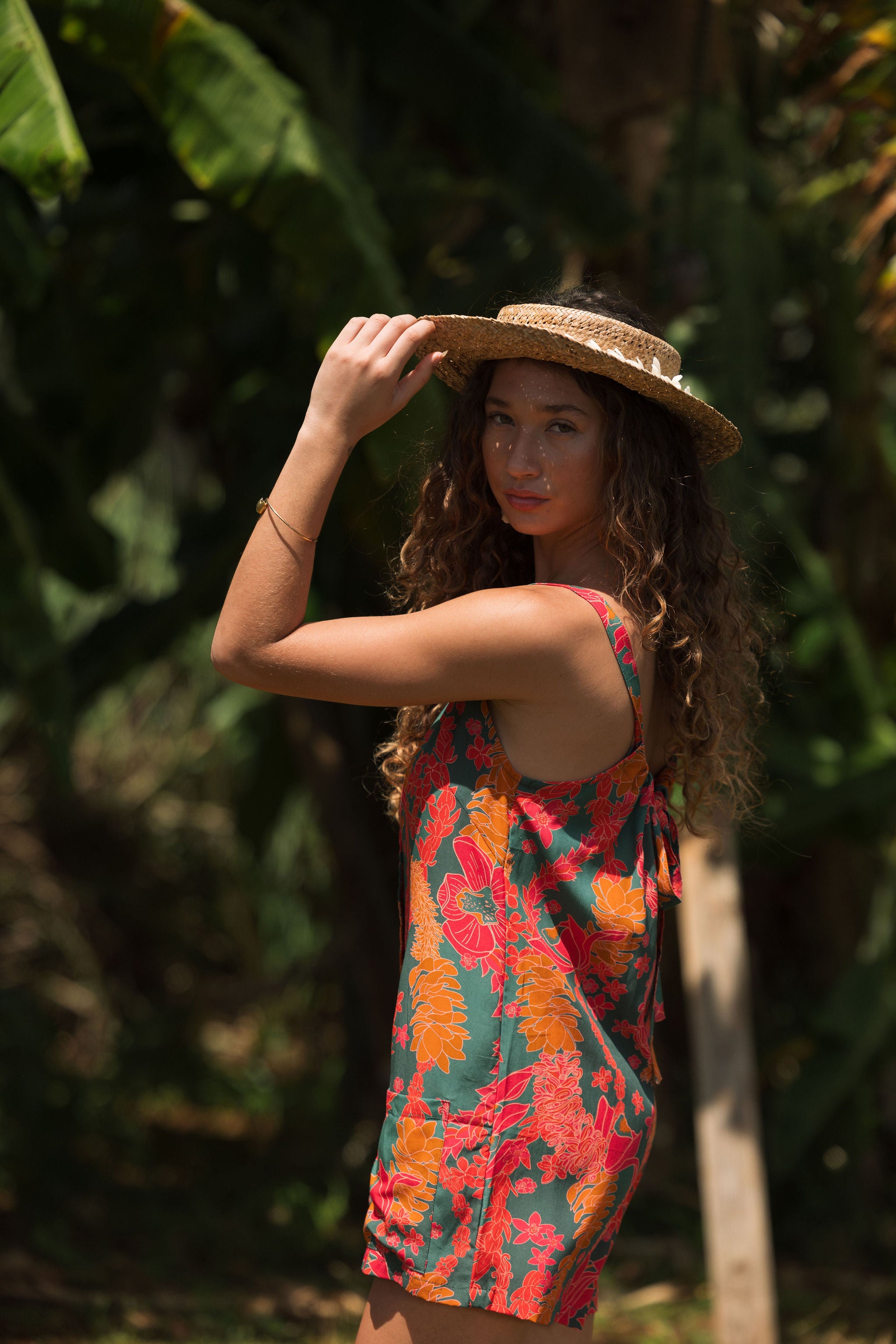 woman with brown hair wearing a colorful romper with tropical lei print