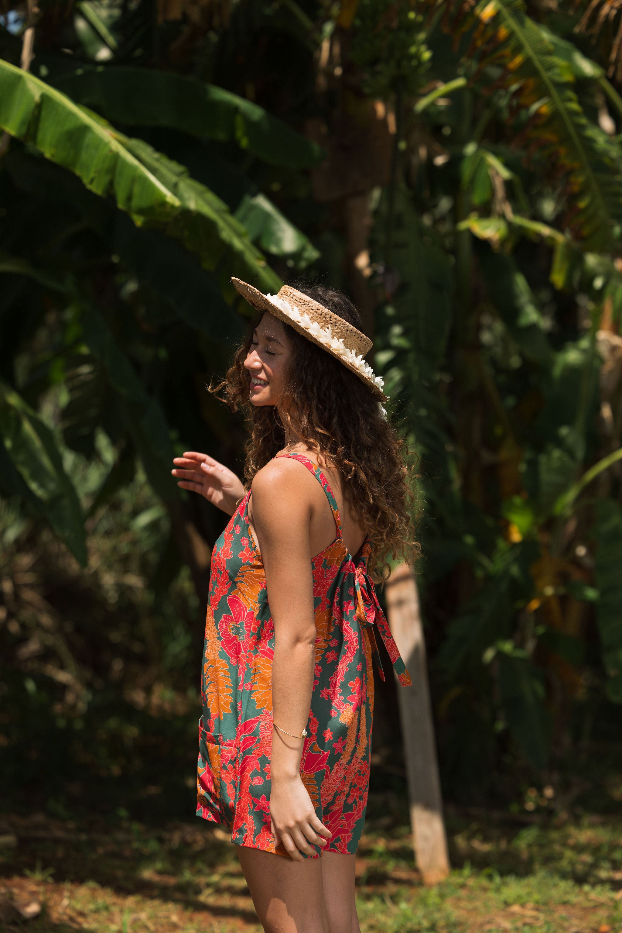 woman with brown hair wearing a colorful romper with tropical lei print