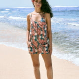 woman with brown hair wearing a blue thin strap tie back romper with red ginger and tiare print.